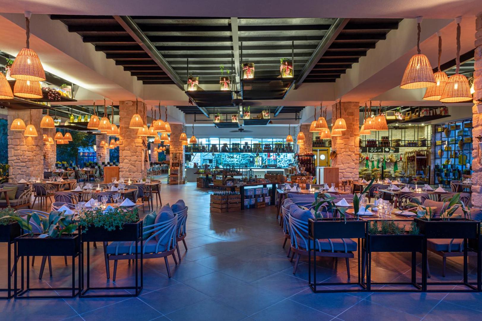 Selectum Family Resort Belek mājīgais restorāns ar siltu apgaismojumu, pītiem gaismekļiem un akmens kolonnām — eleganta vakariņu zona ar mīkstiem krēsliem
