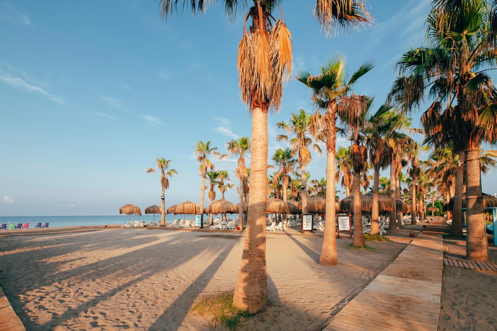 Plaša Selectum Family Resort Belek smilšu pludmale ar palmām, koka laipām un saulessargiem pie dzidri zilās Vidusjūras
