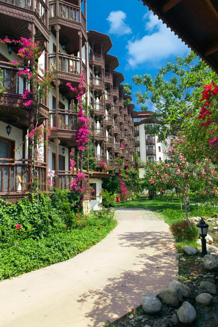 Selectum Family Resort Belek numuru korpuss ar koka balkoniem un ziedošiem bugenvillu krūmiem dārza ielokā