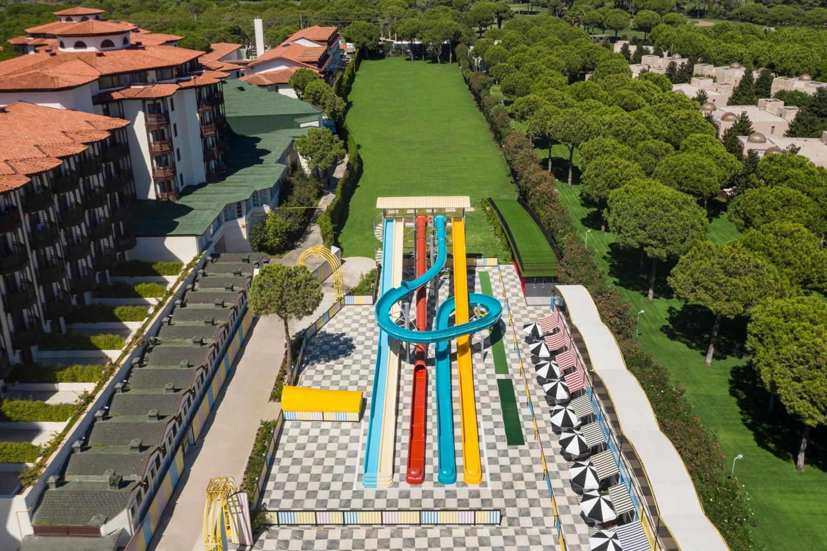 Selectum Family Resort Belek teritorijas skats ar lielajiem ūdens slidkalniņiem, viesnīcas ēku un apkārtējo priežu mežu Belekā