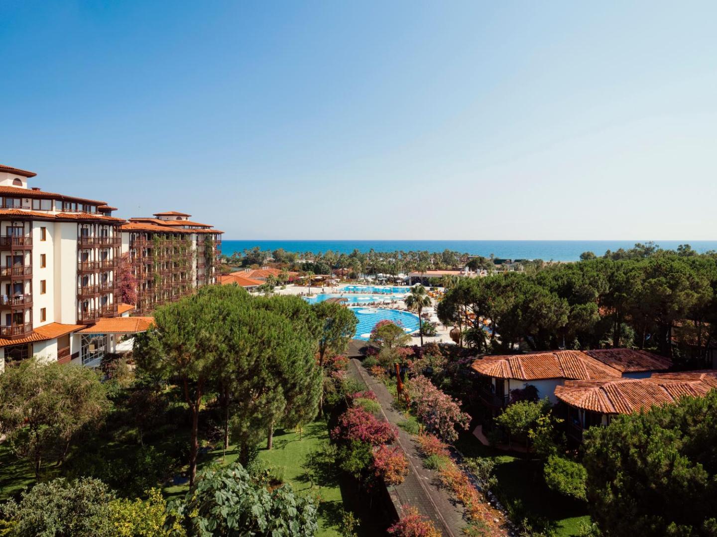 Skats no Selectum Family Resort Belek augšējiem stāviem uz baseinu zonu, priežu mežu un Vidusjūras horizontu