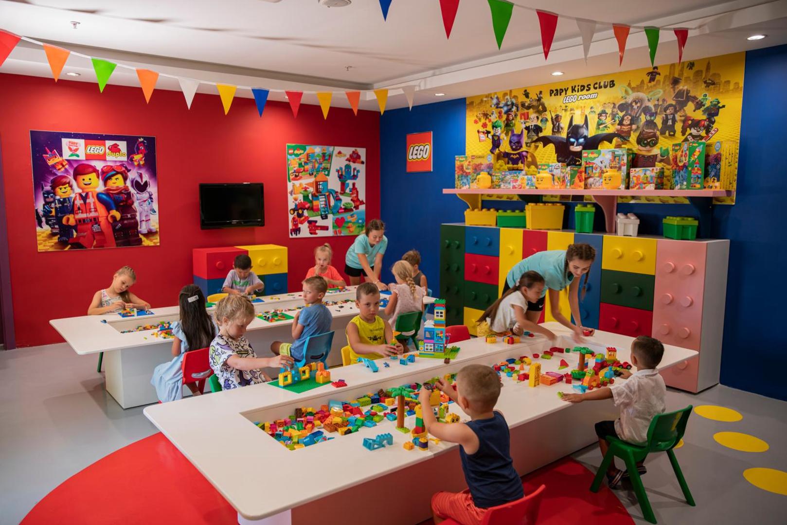 Papillon Ayscha bērnu kluba LEGO istaba ar krāsainiem galdiem, klučiem un bērniem, kas spēlējas animatoru uzraudzībā