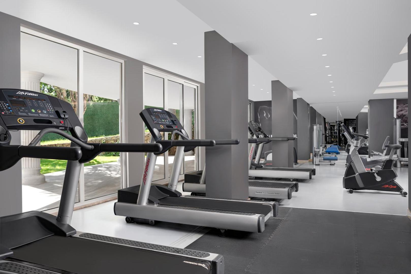 Papillon Belvil modernais fitness centrs ar Life Fitness skrejceliņiem un trenažieriem Belekā — gaiša sporta zāle ar skatu uz dārzu