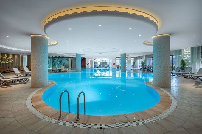 Papillon Belvil iekštelpu spa baseins ar modernu apgaismojumu, kolonnām un ērtiem atpūtas krēsliem relaksācijai Belekas kūrortā.