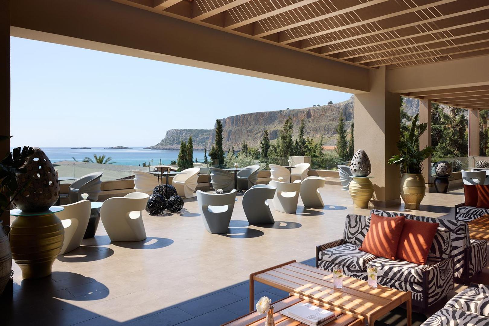 Aquagrand Exclusive Deluxe Resort atpūtas zona ar dizaina mēbelēm un skatu uz klintīm un jūru Rodas piekrastē — saulaina terase ar nojumi