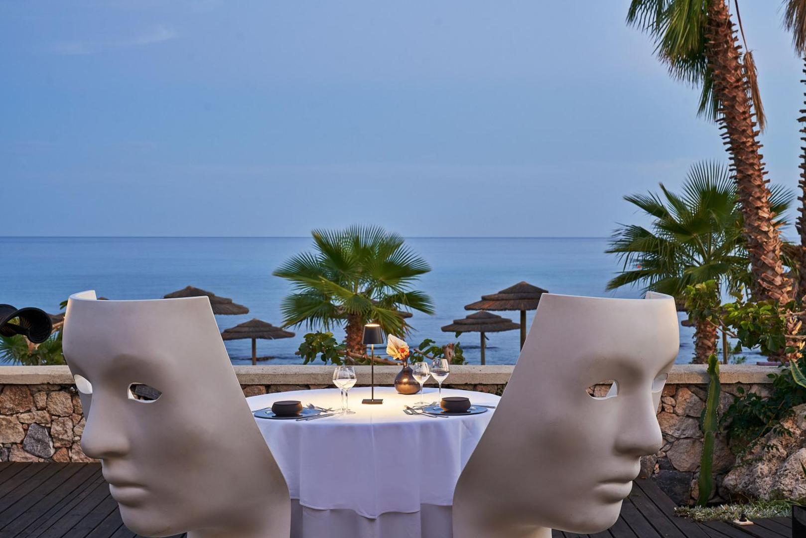 Aquagrand Exclusive Deluxe Resort restorāna galdiņš ar unikāliem sejas formas krēsliem saulrieta laikā Rodā
