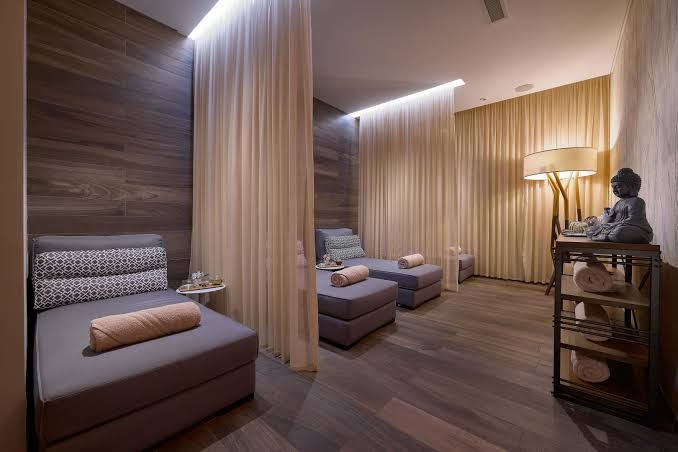 The Chedi Lustica Bay spa centra atpūtas telpa ar mīkstiem zviļņiem, koka apdari un gaismas caurlaidīgiem aizkariem