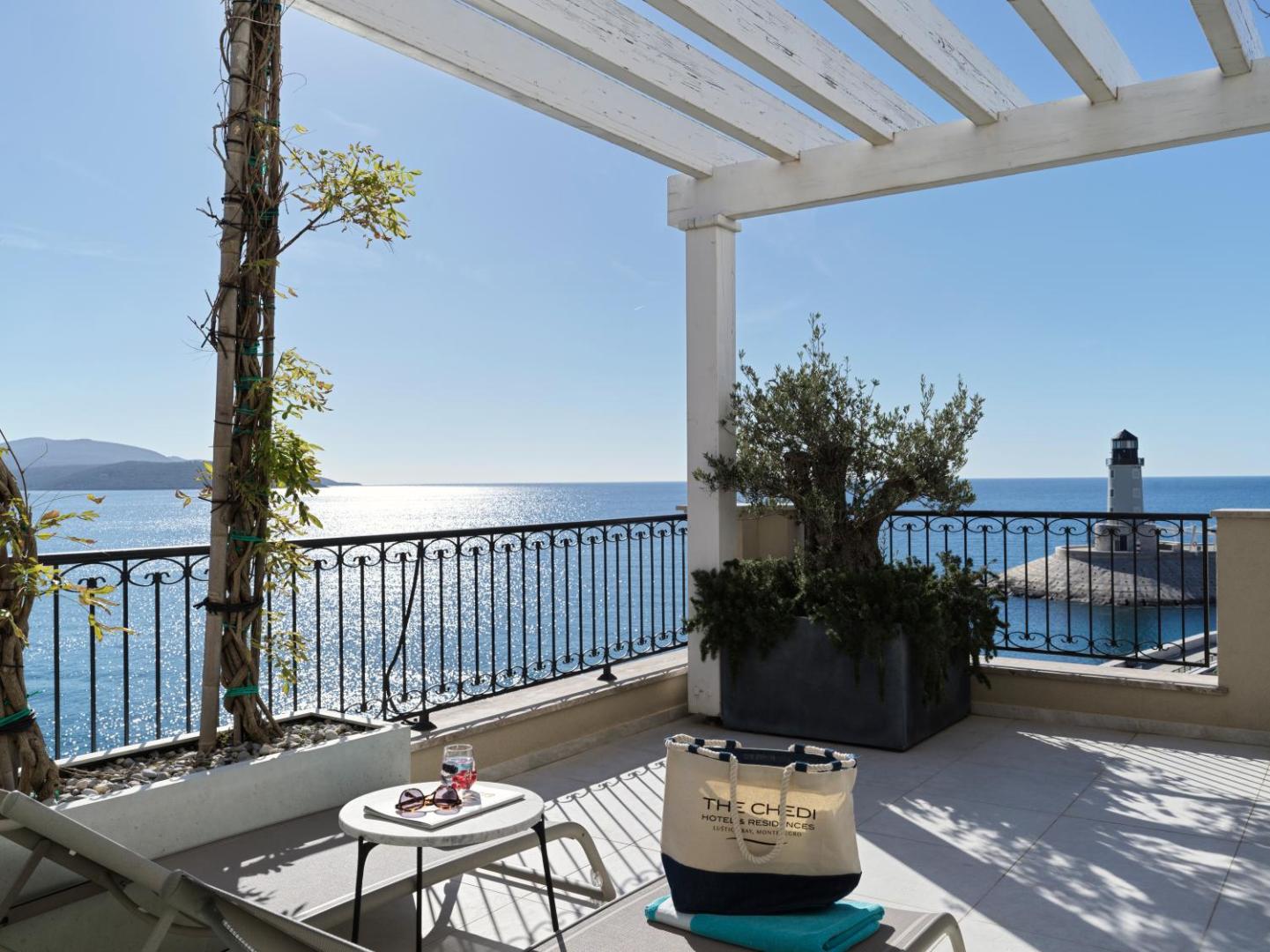 The Chedi Lustica Bay numura terase ar skatu uz jūru un bāku — saules krēsli, olīvkoks podā un balta koka pergola
