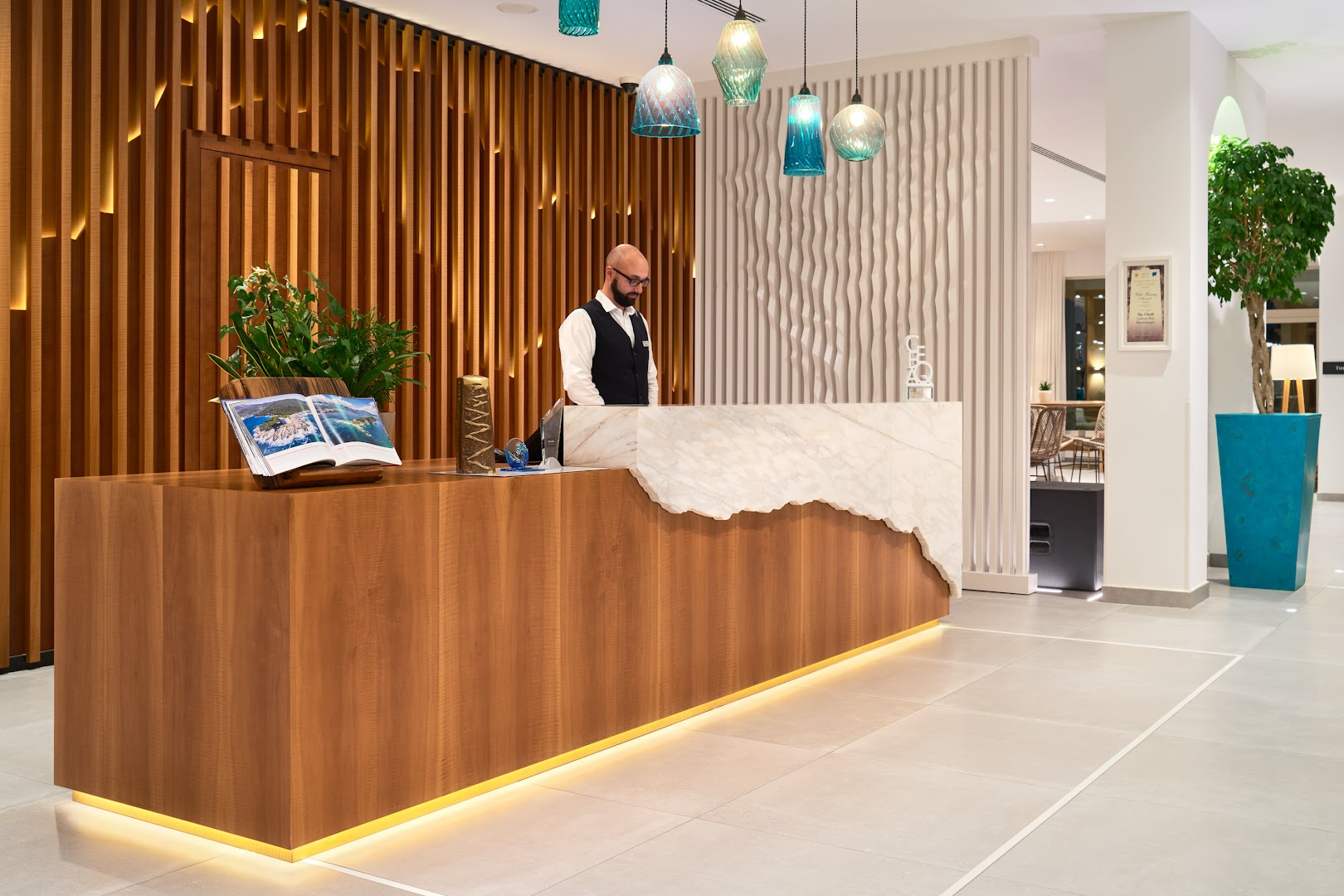 The Chedi Lustica Bay viesnīcas recepcijas lete ar marmora apdari un koka elementiem, kur viesus sagaida darbinieks
