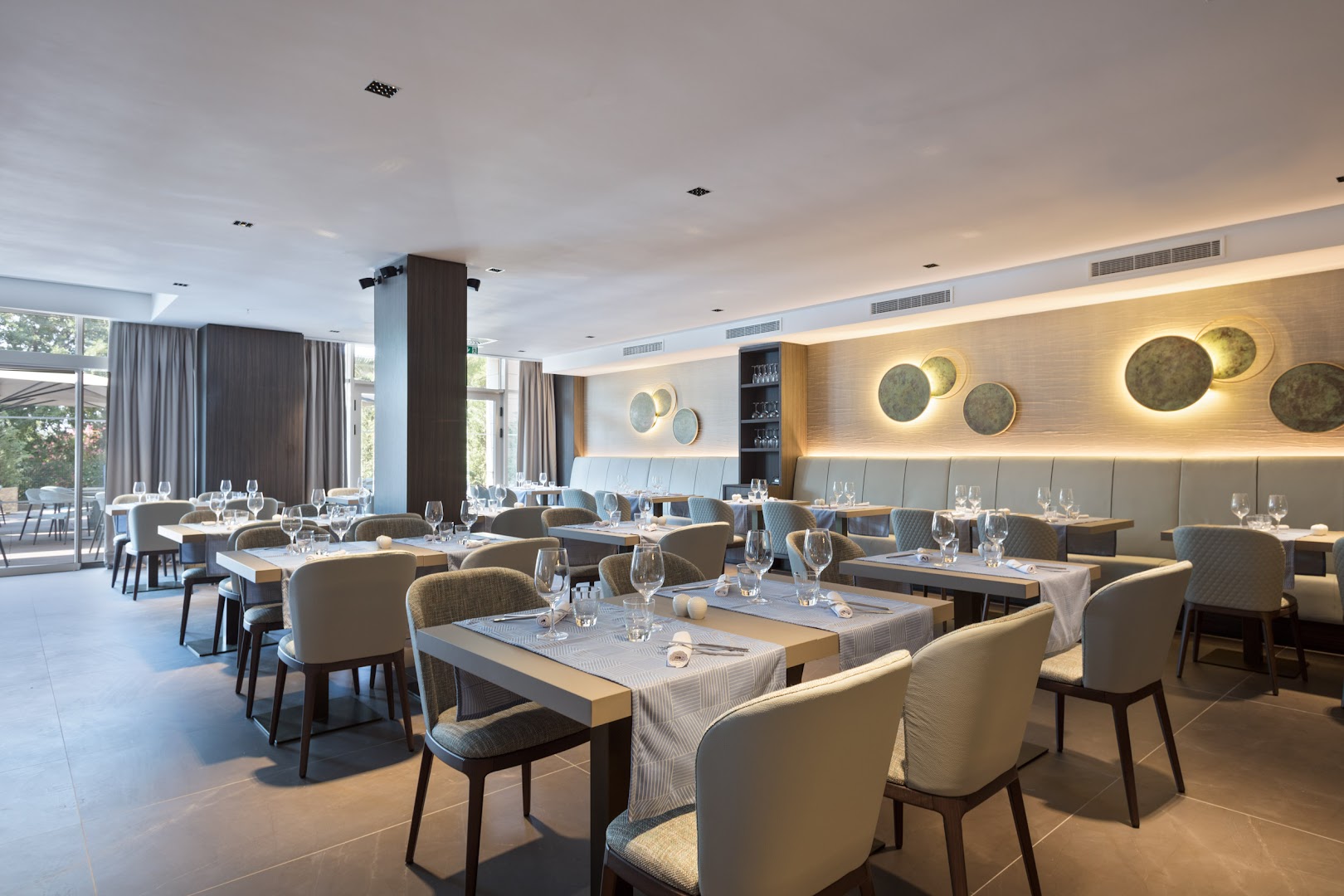 Hotel Ami Budva Petrovac restorāna interjers ar eleganti klātiem galdiem, mīkstiem krēsliem un modernu apgaismojumu Petrovacā, Melnkalnē.