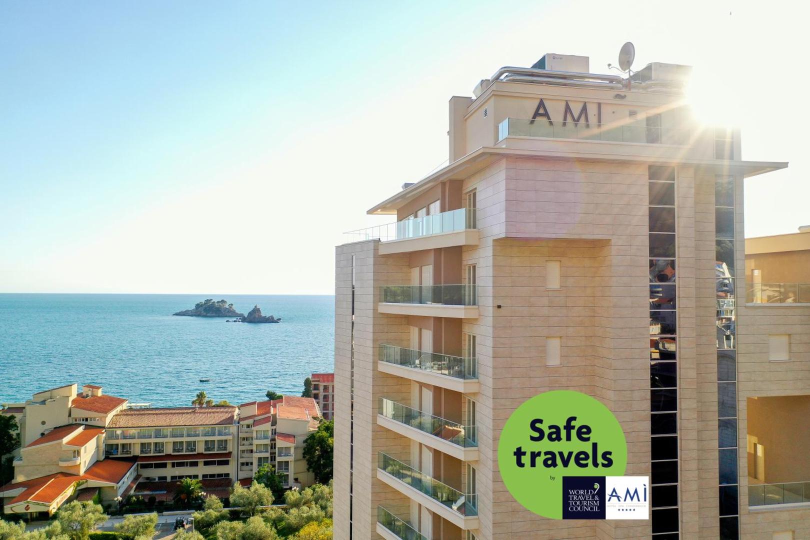 Hotel Ami Budva Petrovac augšējie stāvi saules gaismā ar skatu uz jūru un Safe Travels drošības sertifikāta logo