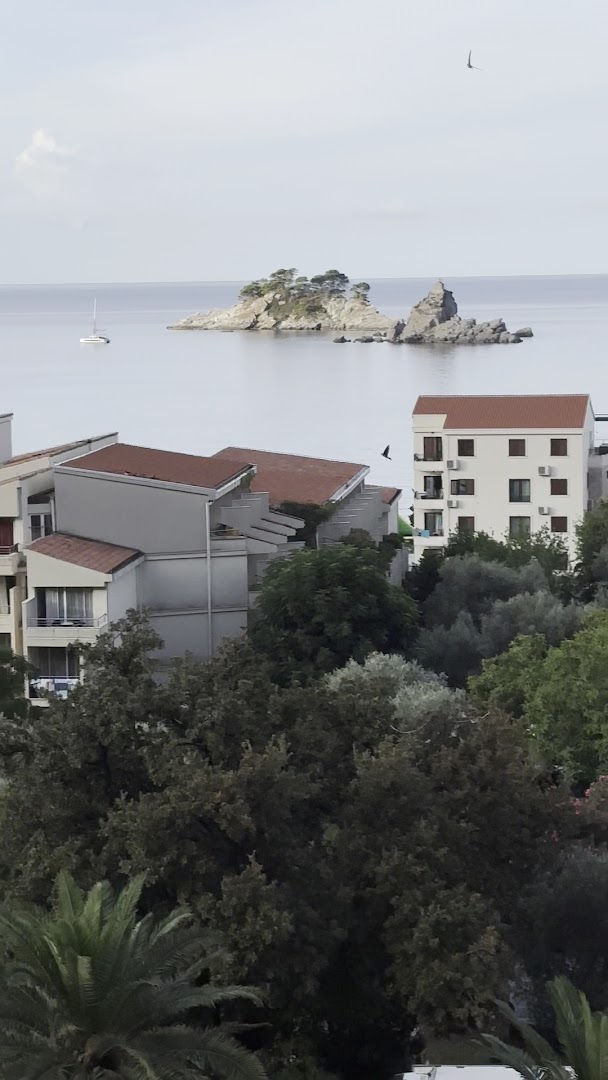 Skats no Hotel Ami Budva Petrovac numura uz Adrijas jūru un klinšainām salām Petrovacas piekrastē, Melnkalnē caur koku galotnēm.