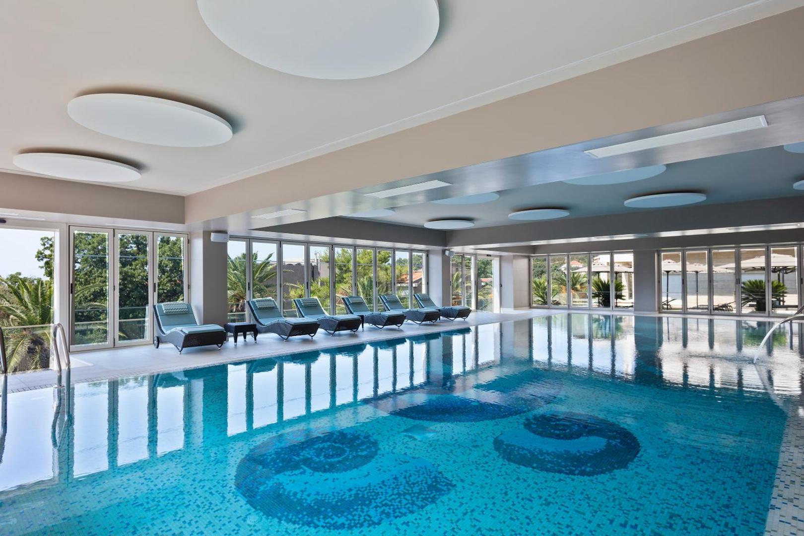 Gaišs Hotel Ami Budva Petrovac spa zonas baseins ar ērtiem zviļņiem un skatu uz dārzu caur panorāmas logiem