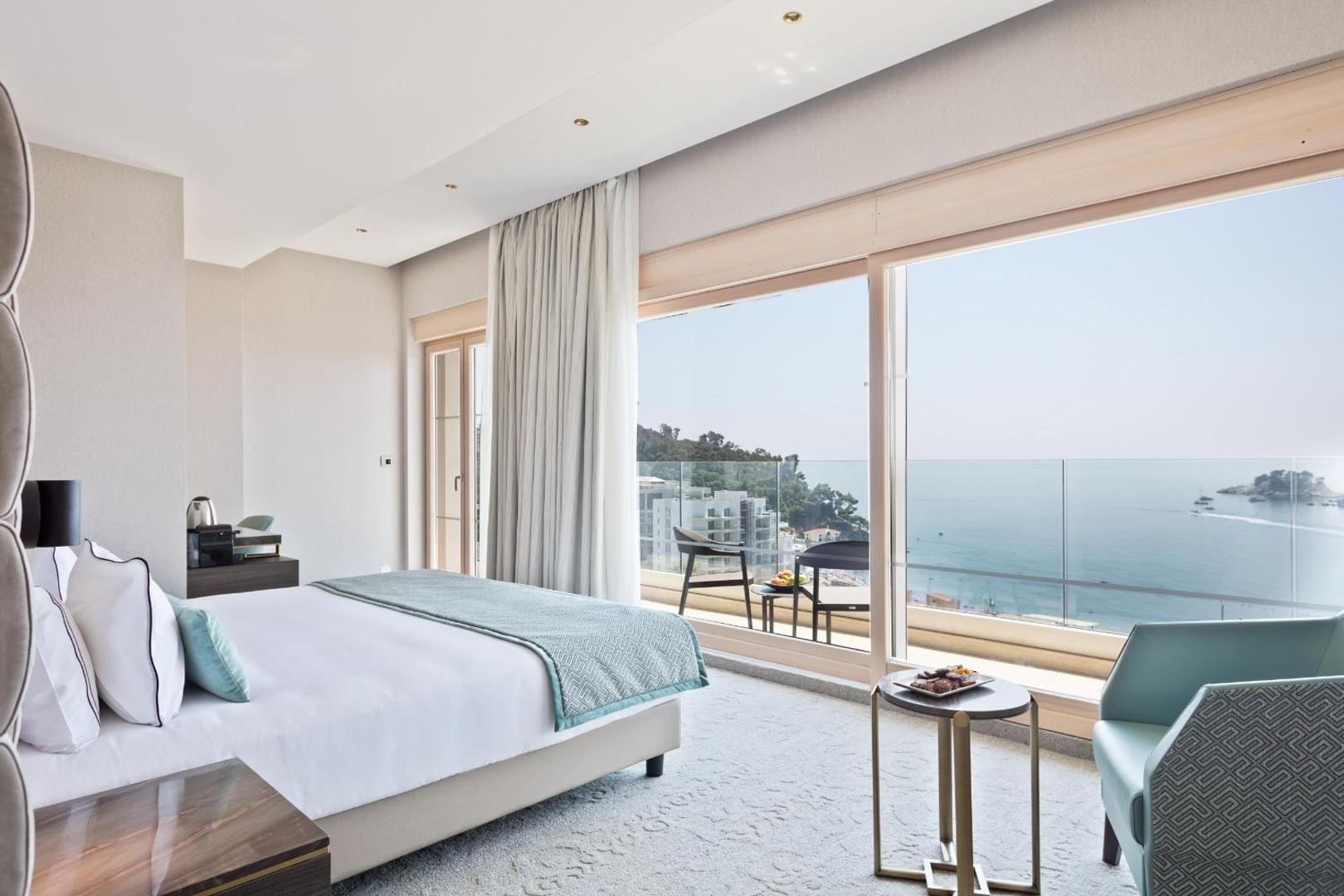 Hotel Ami Budva Petrovac gaišs numurs ar lielu divguļamo gultu un panorāmas logu, no kura paveras skats uz Adrijas jūru.