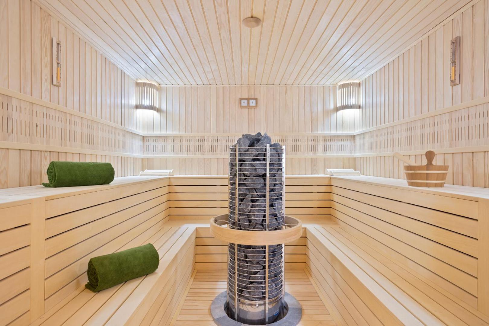 Hotel Ami Budva Petrovac moderna sauna ar gaiša koka apdari, centrālo akmens krāsni un zaļiem dvieļiem relaksācijai spa zonā
