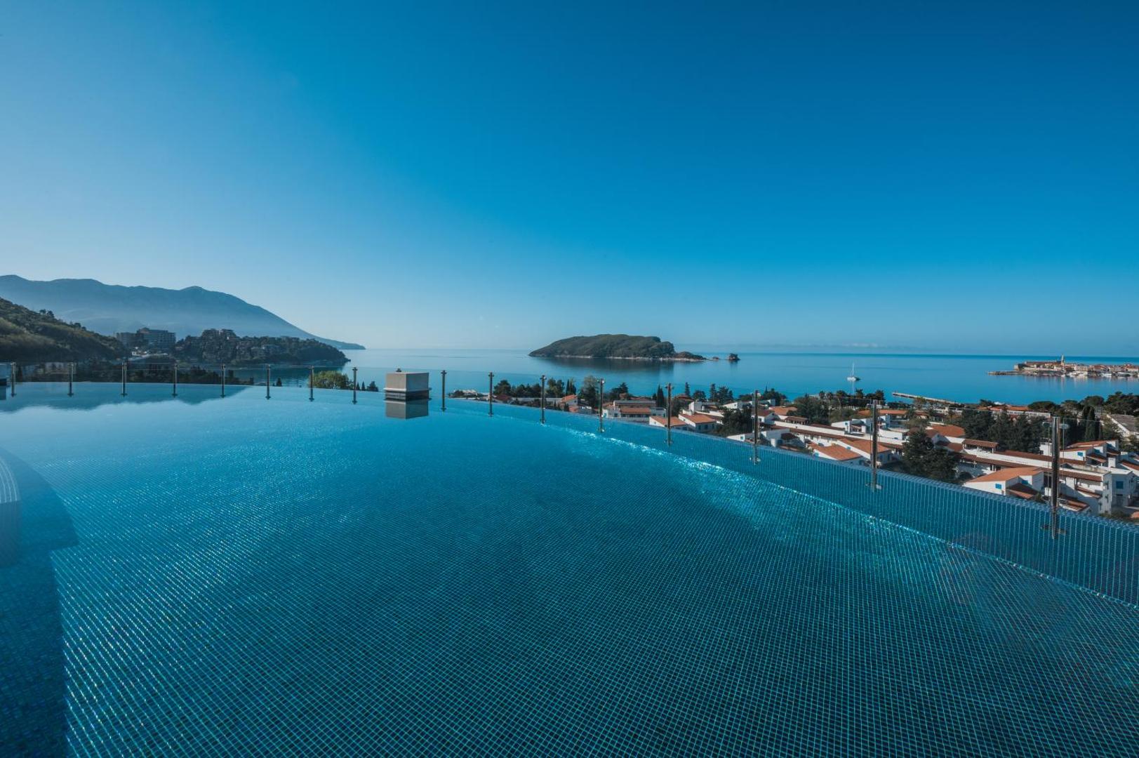 Iberostar Waves Slavija infinity baseins uz jumta ar skatu uz Budvas vecpilsētu un jūras horizontu zilās debesīs