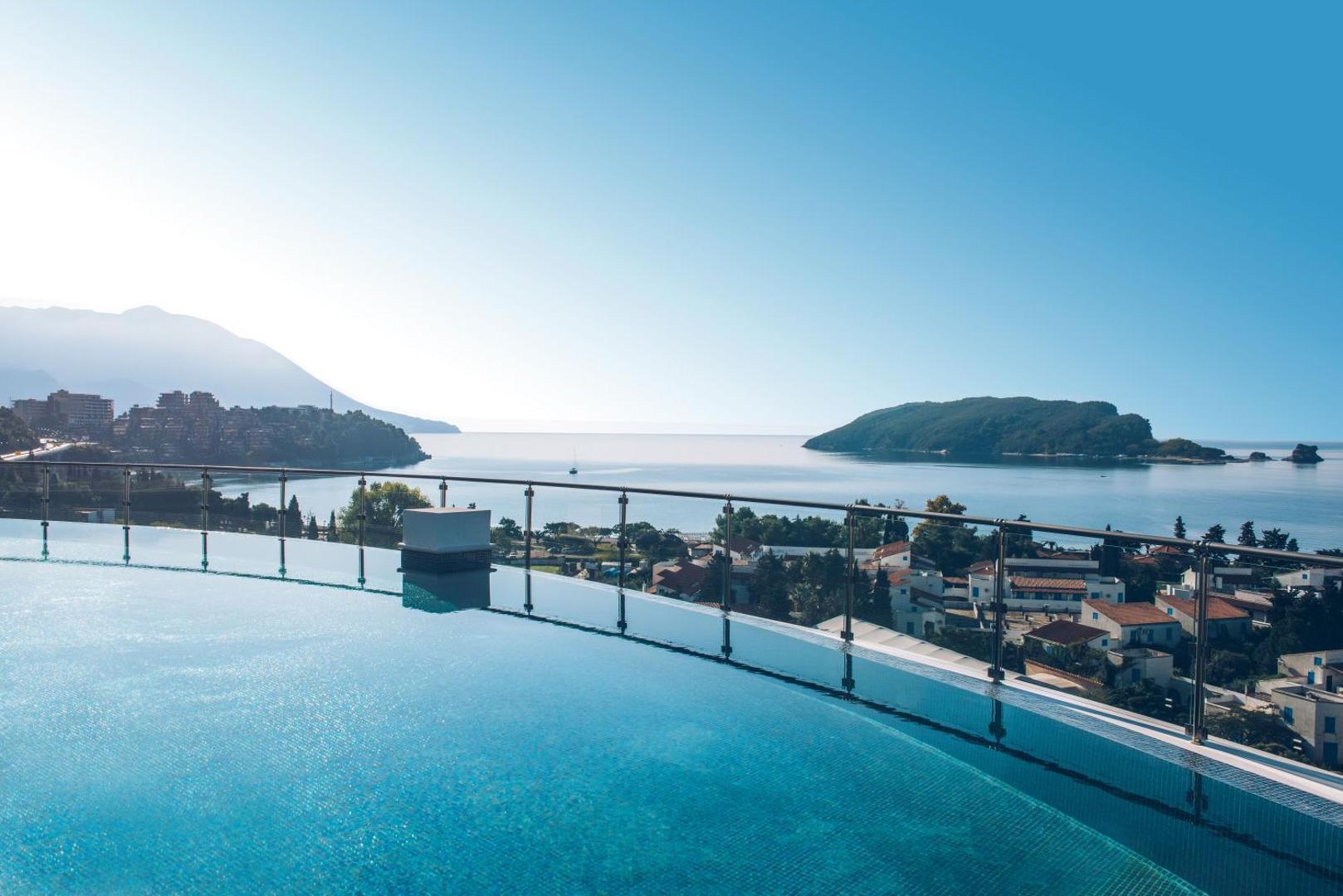 Iberostar Waves Slavija bezmalas baseins uz jumta ar skatu uz Budvas līci un salu Melnkalnē saulainā dienā