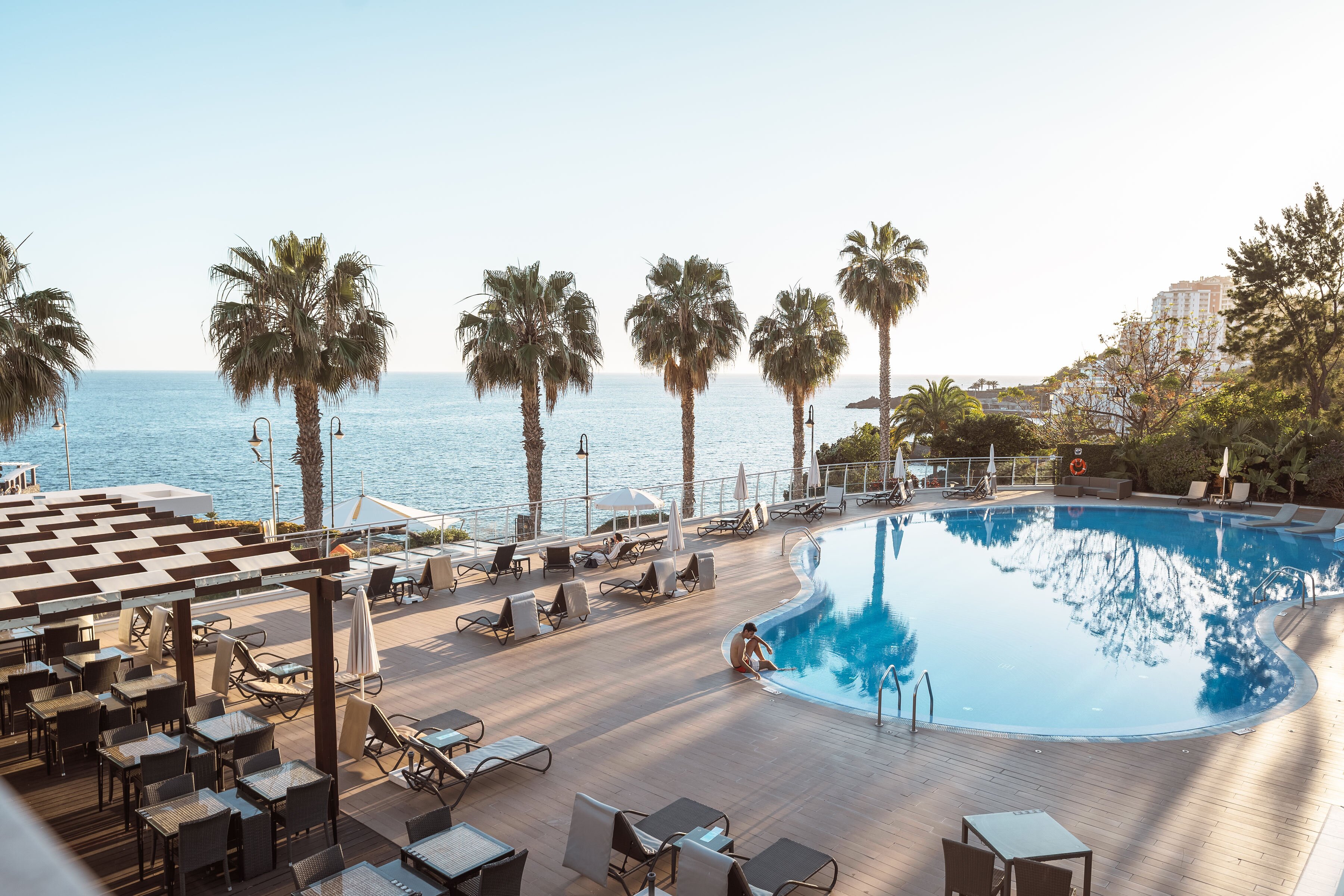 Baseins ar skatu uz jūru, apkārt palmām un saulessargiem, radot relaksējošu atmosfēru. Ideāla vieta atpūtai un atjaunošanai. panoramic view with beach and pools