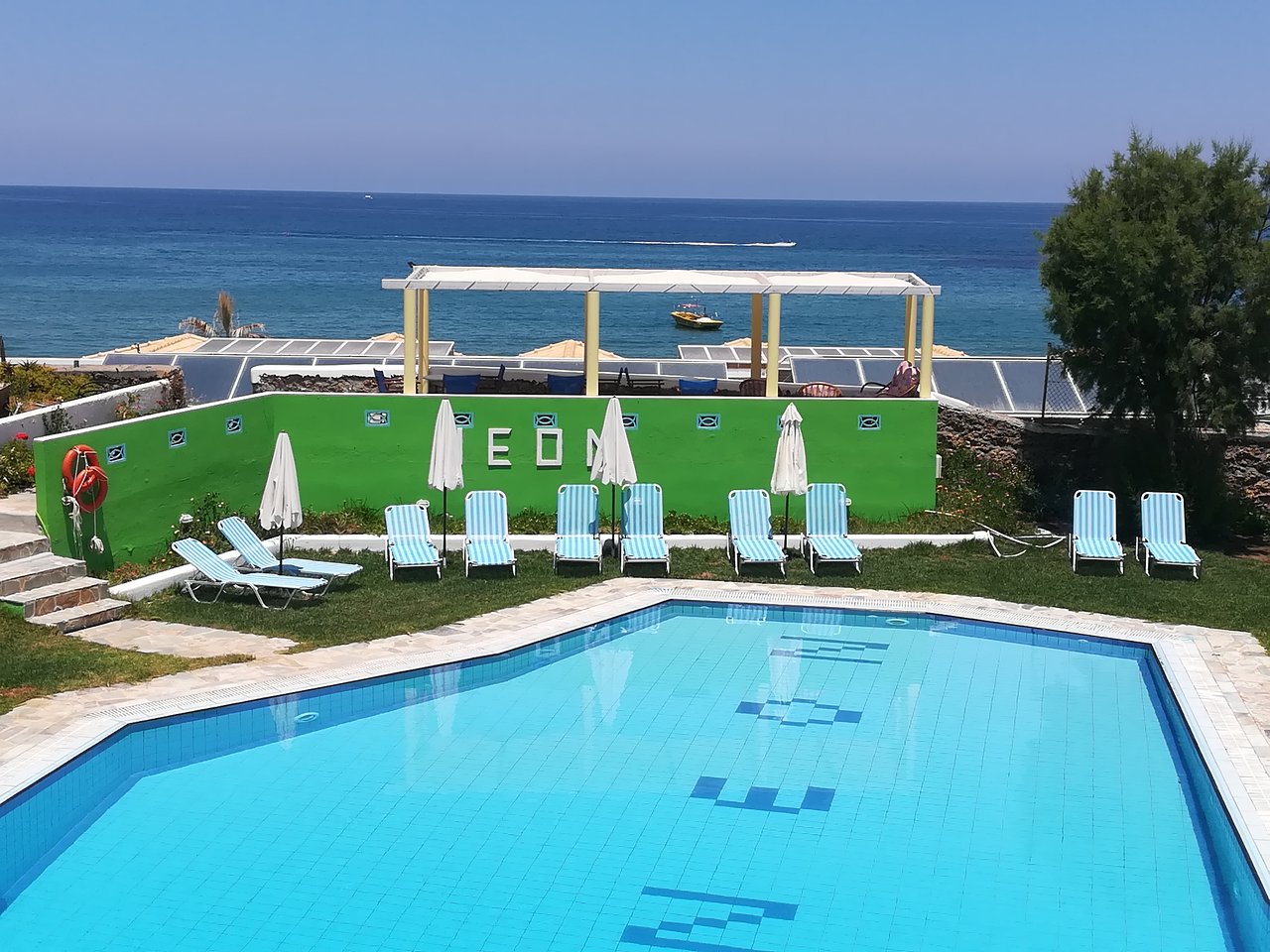 Peldbaseins ar saulessargiem un guļamkrēsliem, blakus zaļš sienas elements, un skats uz jūru. Ideāla vieta relaksācijai un atpūtai. panoramic view with beach and pools