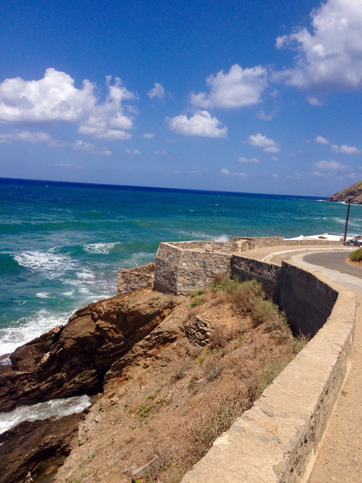 Krasta ainava ar klintīm un zilo jūru, kur viļņi sitas pret akmeņiem. Debesis skaidras ar baltām mākoņu pūkām. panoramic view with beach and pools