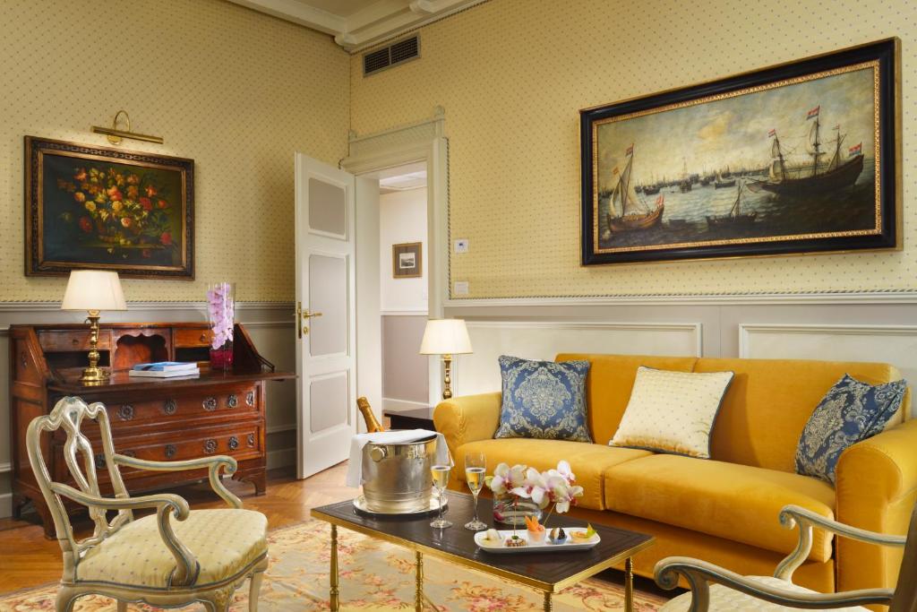Mūsdienīgs viesnīcas numurs ar dzeltenu dīvānu, elegantu mēbeļu kombināciju un mākslas darbiem uz sienām, radot mājīgu atmosfēru.