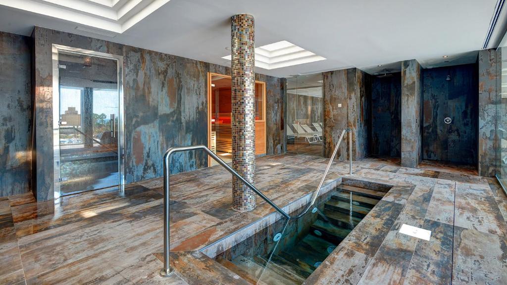 Mūsdienīgs spa telpas interjers ar metāliskām un akmens tekstūrām, kas ietver baseinu un dušas zonas. Ideāla vide relaksācijai un atpūtai.
