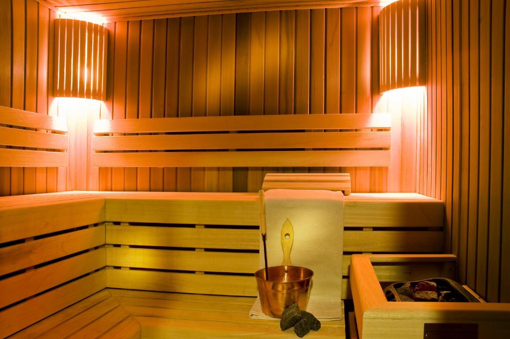 Mūsdienīga koka sauna ar siltu apgaismojumu, kas rada relaksējošu atmosfēru. Redzams koka trauks un dvielis, kas papildina interjeru.