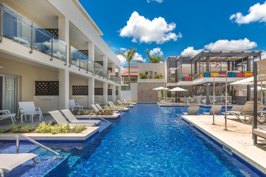 Mūsdienīgs viesnīcas komplekss ar baseinu, saulessargiem un atpūtas zonām, ideāla vide relaksācijai. Skats uz zilo debesi un baltiem mākoņiem.