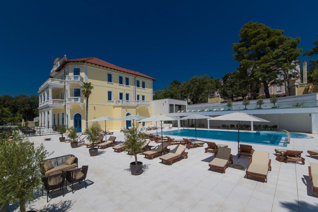 Viesnīca ar dzeltenām sienām un sarkanu jumtu, apkārtējā teritorijā ir peldbaseins un sauļošanās krēsli. Apkārt ir zaļi koki un sauļošanās zonas ar saulessargiem.