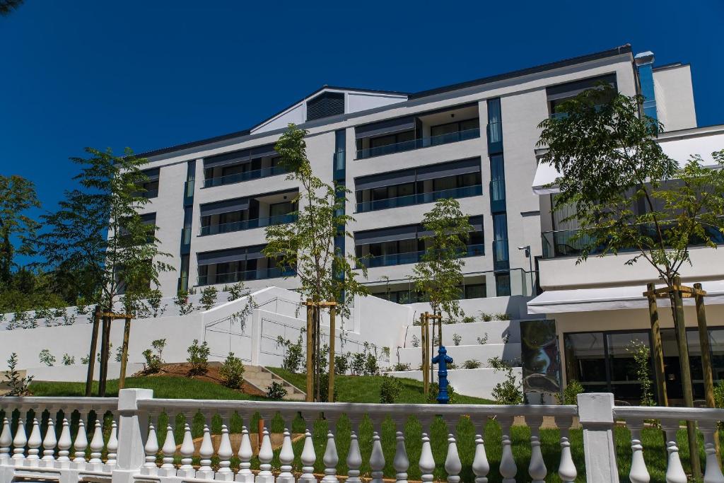 Mūsdienīga trīsstāvu ēka ar plašām terasēm un zaļo teritoriju apkārt. Apkārtnē redzami jauni koki un sakopta zāliena zona.