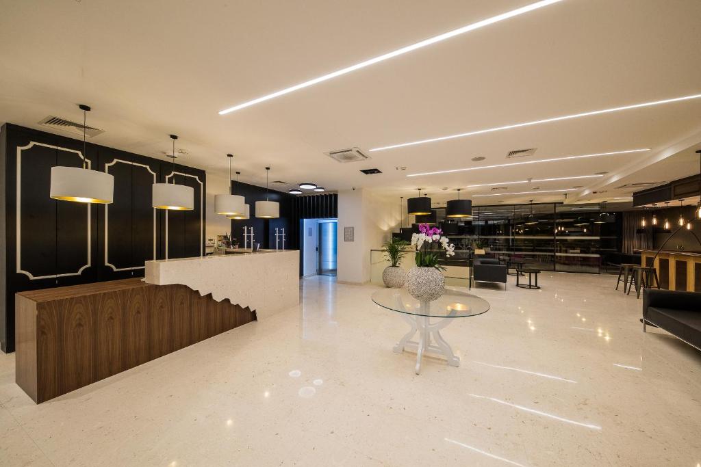 Mūsdienīgs viesnīcas reģistratūras interjers ar elegantu apgaismojumu un stilīgu mēbelējumu, kas rada viesmīlīgu atmosfēru. Galda centrā ir dekoratīvas ziedu kompozīcijas.