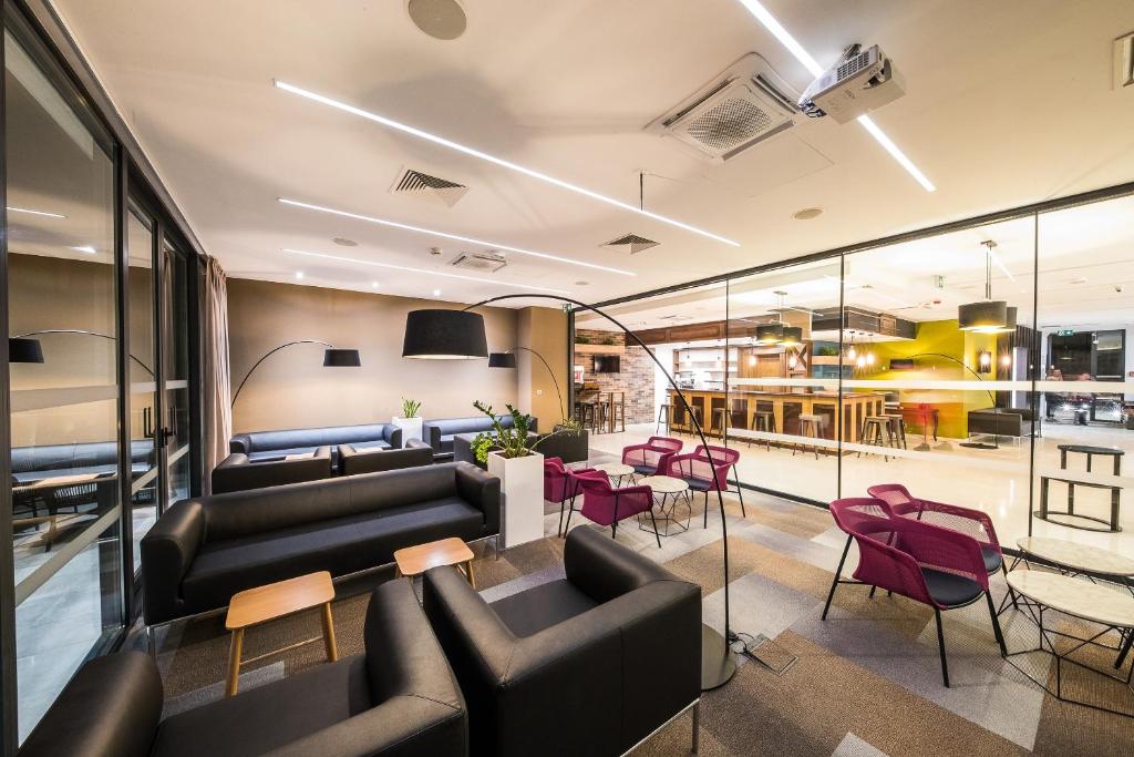 Mūsdienīgs un stilīgs atpūtas zonas dizains ar melniem dīvāniem, rozā krēsliem un plašu galdu, radot ērtu atmosfēru. Gaismas elementi un stikla sienas piešķir telpai modernu izskatu.