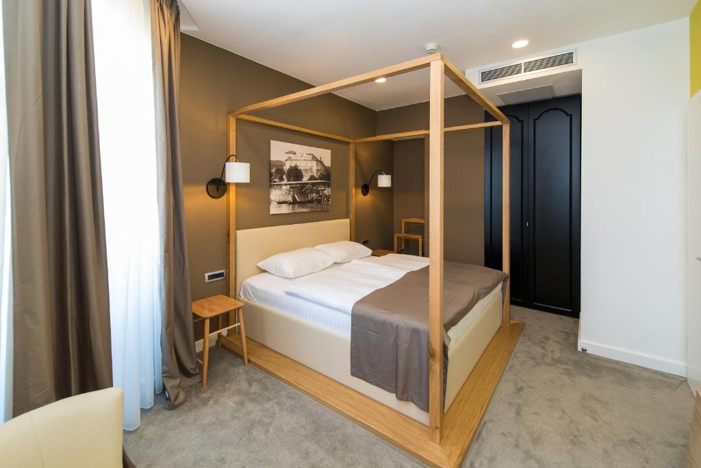 Mūsdienīga guļamistaba ar četru stūru gultu, dabīgā koka konstrukciju un neitrālām sienām, radot relaksējošu atmosfēru. Logi ar aizkariem ļauj ieplūst dabiskajai gaismai.