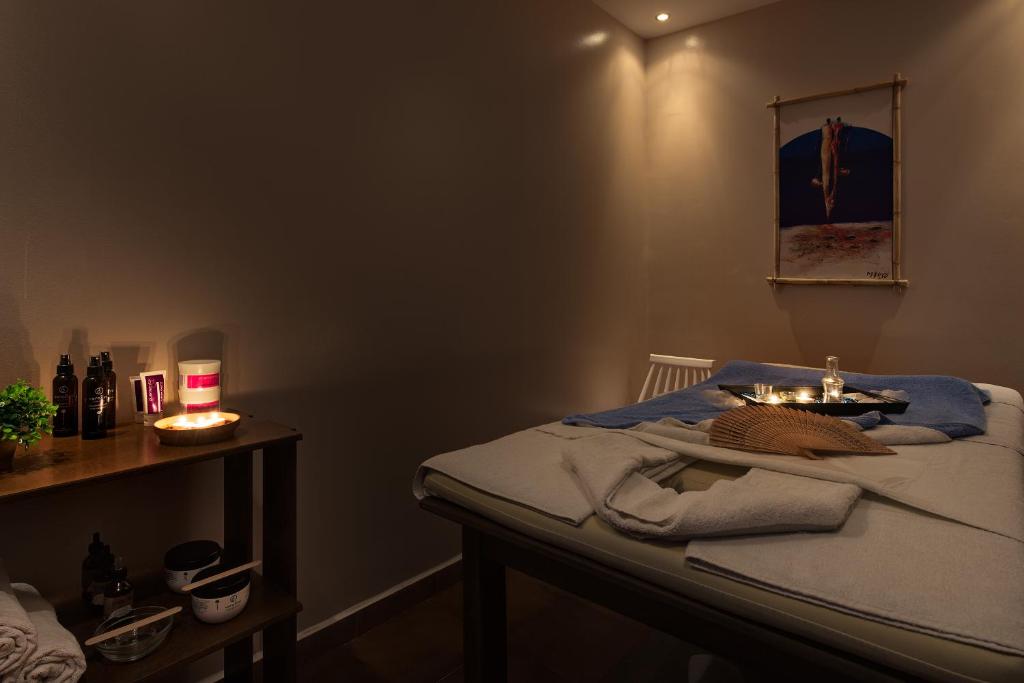 Mierīga un relaksējoša spa telpa ar masāžas galdu, aromātiskām svecēm un kosmētikas produktiem. Siltas gaismas un mākslas darbs rada patīkamu atmosfēru.