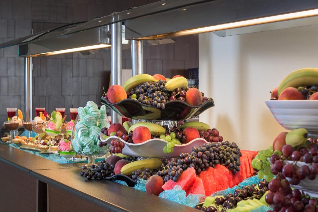Bagātīgs augļu bufete ar dažādiem augļiem, tostarp vīnogām, āboliem un banāniem, kā arī saldumiem un desertiem. Ideāla izvēle veselīgai uzkodu baudīšanai.
