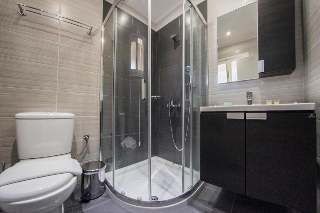 Mūsdienīgs vannas istabas interjers ar stikla dušas kabīni, tualeti un melnu skapīti, kas nodrošina elegantu un funkcionālu telpu. Apgaismojums un flīžu dizains piešķir šai telpai modernu izskatu.
