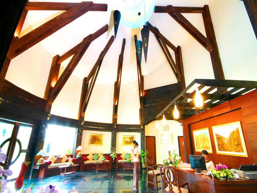 Mūsdienīgs un elegants viesnīcas reģistratūras interjers ar augstiem koka griestiem un ziedu dekorācijām, radot siltu un viesmīlīgu atmosfēru.