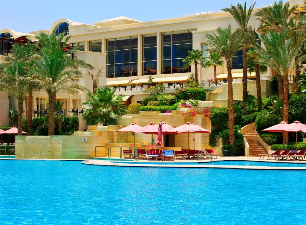 Grand Rotana Resort & Spa baseins ar palmām un saules nojumi