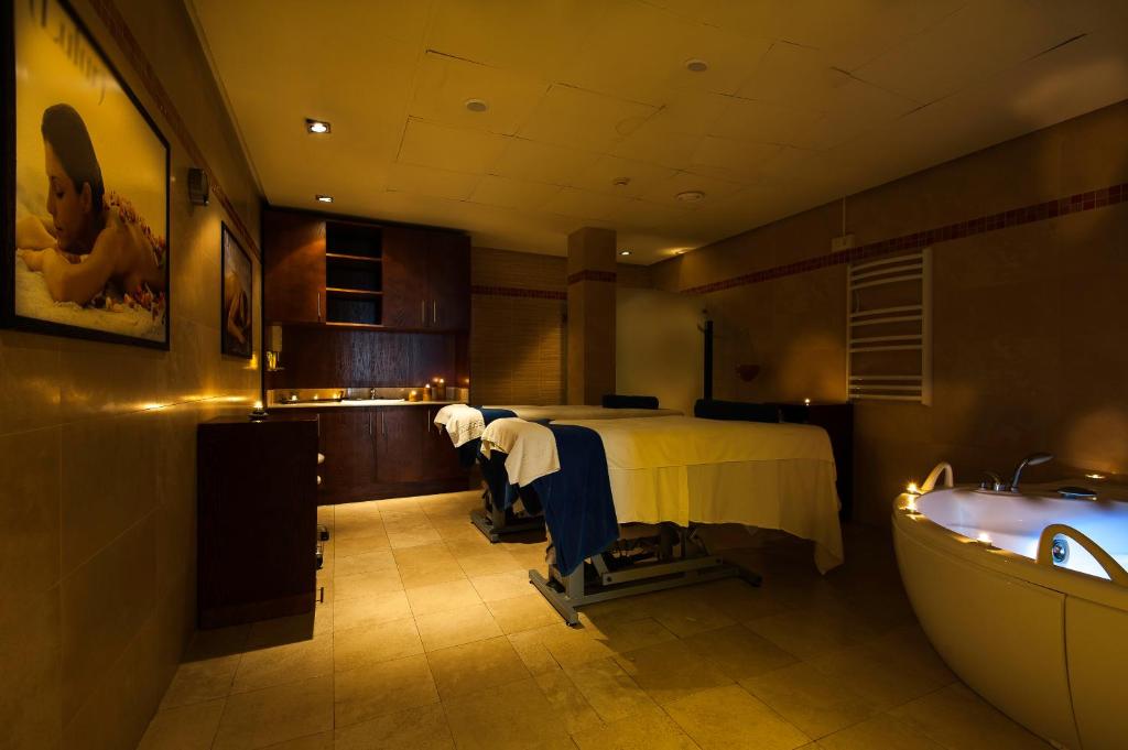 Mūsdienīgs spa interjers ar masāžas galdiem, apgaismojumu un relaksējošu atmosfēru. Telpā ir redzams arī burbuļvanna un skapji.