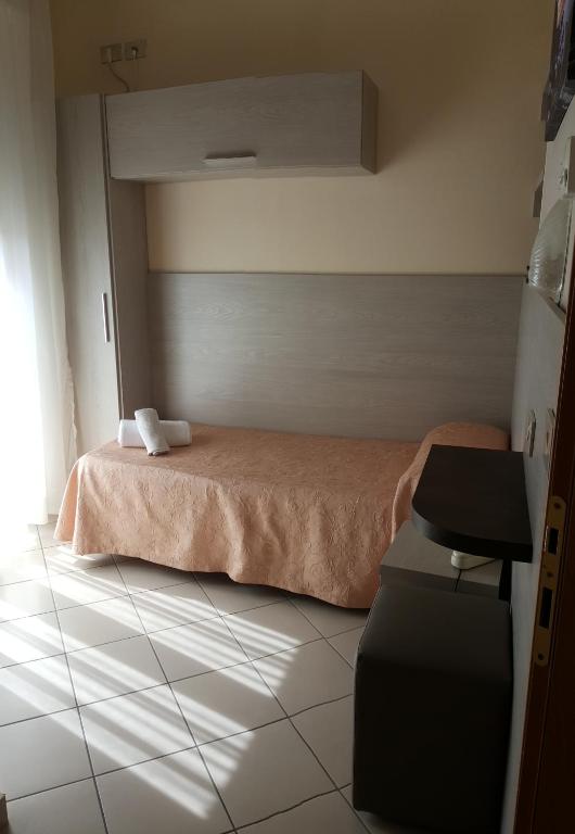 Mūsdienīga viesnīcas numura interjers ar gultu, apgaismotas grīdas flīzes un logu, caur kuru ieplūst dienas gaisma. Uz gultas novietoti dvieļi un ir redzami moderni mēbeļu elementi.