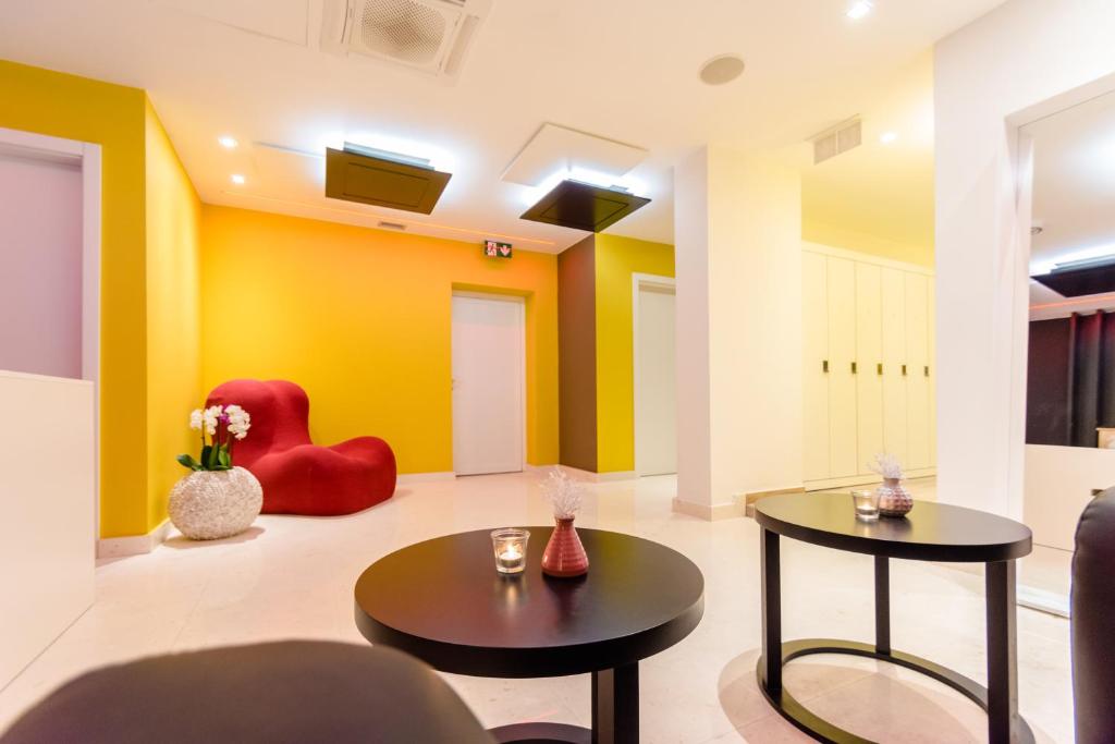 Mūsdienīgs un krāsains interjers ar dzeltenām un sarkanām sienām, modernām mēbelēm un interjera elementiem. Telpa ir gaiša un aicinoša, ar galdiem un dekoratīviem elementiem.