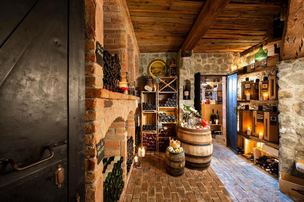 Vīna pagrabs ar akmens un koka elementiem, kurā redzami dažādi vīna pudeles, sveces un koka mucas. Siltā un mājīgā atmosfērā izceltas vīna kolekcijas un dekoratīvie elementi.