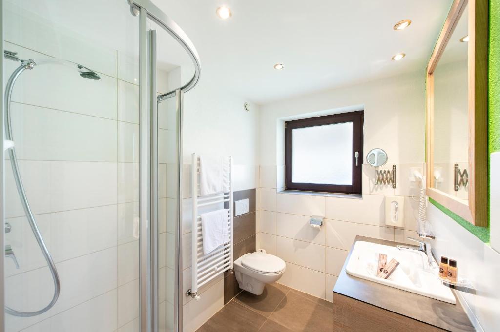 Mūsdienīgs vannas istabas interjers ar dušu, tualeti un izlietni, papildināts ar vannas piederumiem un dabīgiem toņiem.