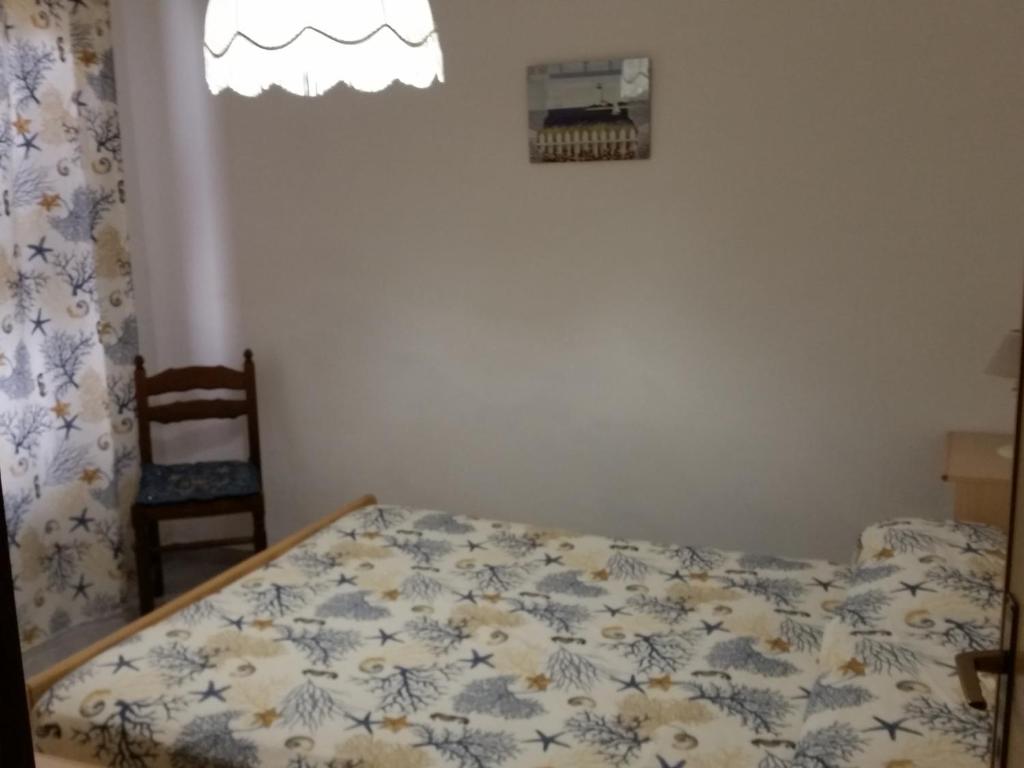 Mierīga guļamistaba ar ziedu raksta gultas veļu, koka krēslu un aizkariem ar jūras motīviem. Gaisma ieplūst caur lampu un logu, radot mājīgu atmosfēru.