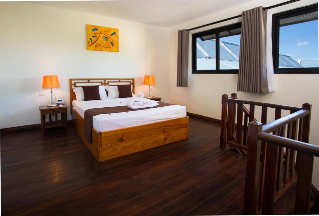 Mūsdienīgs guļamistabas interjers ar koka grīdu, gultu un krāsainām lampām. Telpā ir lieli logi, kas nodrošina dabīgu apgaismojumu.