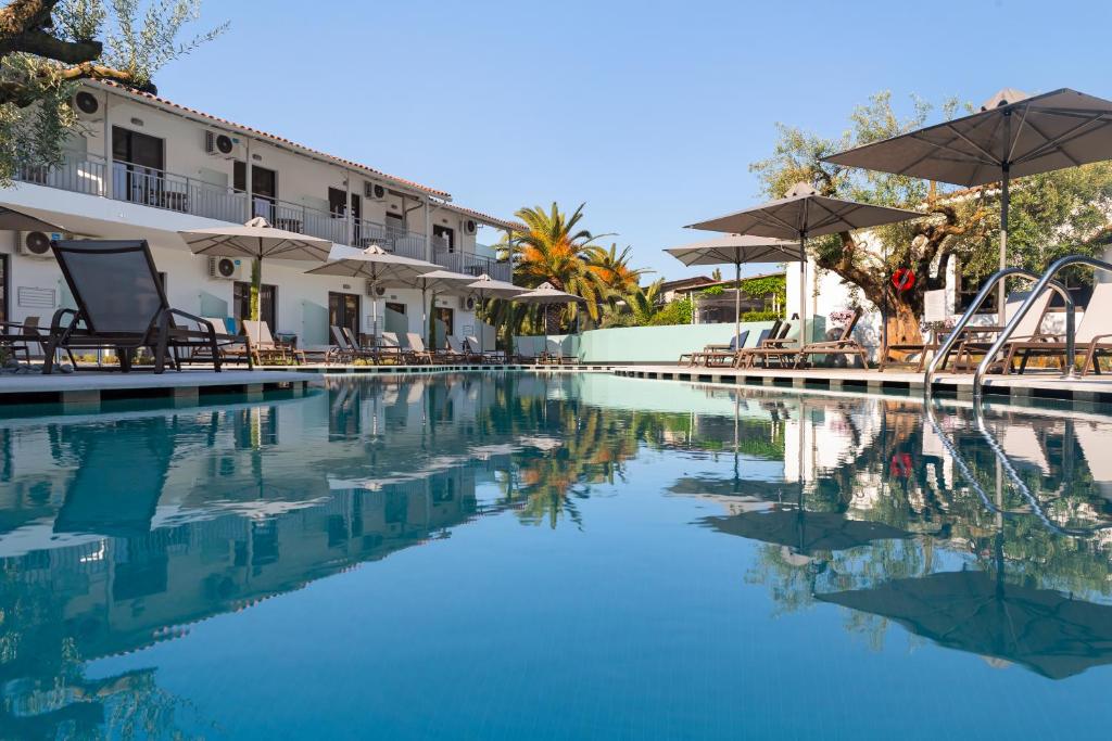 Viesnīcas baseins ar atpūtas krēsliem un saulessargiem, apkārt augoši palmu koki un zaļi stādījumi. Ideāla vieta relaksācijai un atpūtai saulainā dienā.