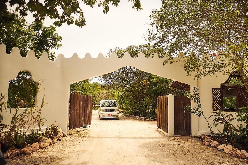 Spice Island Hotel & Resort ieeja ar zaļiem kokiem un baltu vārtu dizainu.