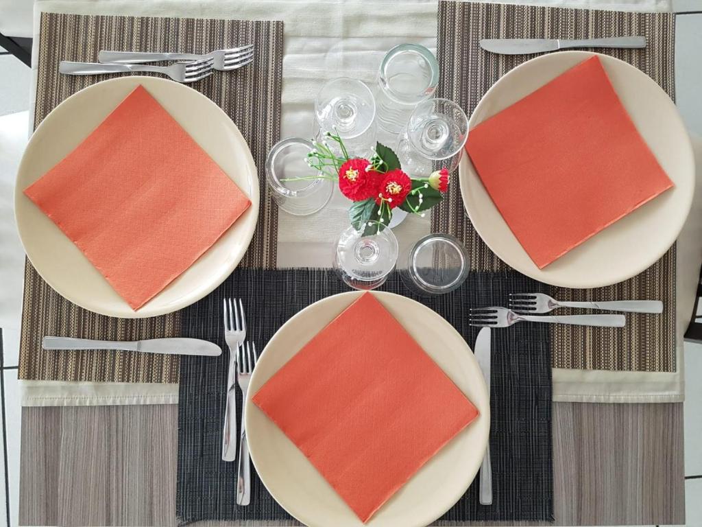 Galda klājums ar divām plāksnēm un oranžiem salvetēm, dekorēts ar ziedu kompozīciju un glāzēm. Ideāls attēls svinīgai maltītei.