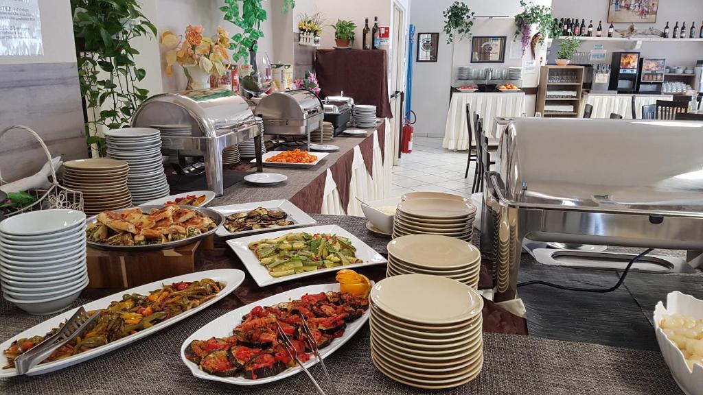 Bagātīgs bufete ar dažādiem ēdieniem, tostarp dārzeņu un gaļas ēdieniem, kā arī šķīvjiem un galda piederumiem. Restorāna iekšiene ar dekoratīviem elementiem un apkalpošanas zonu.