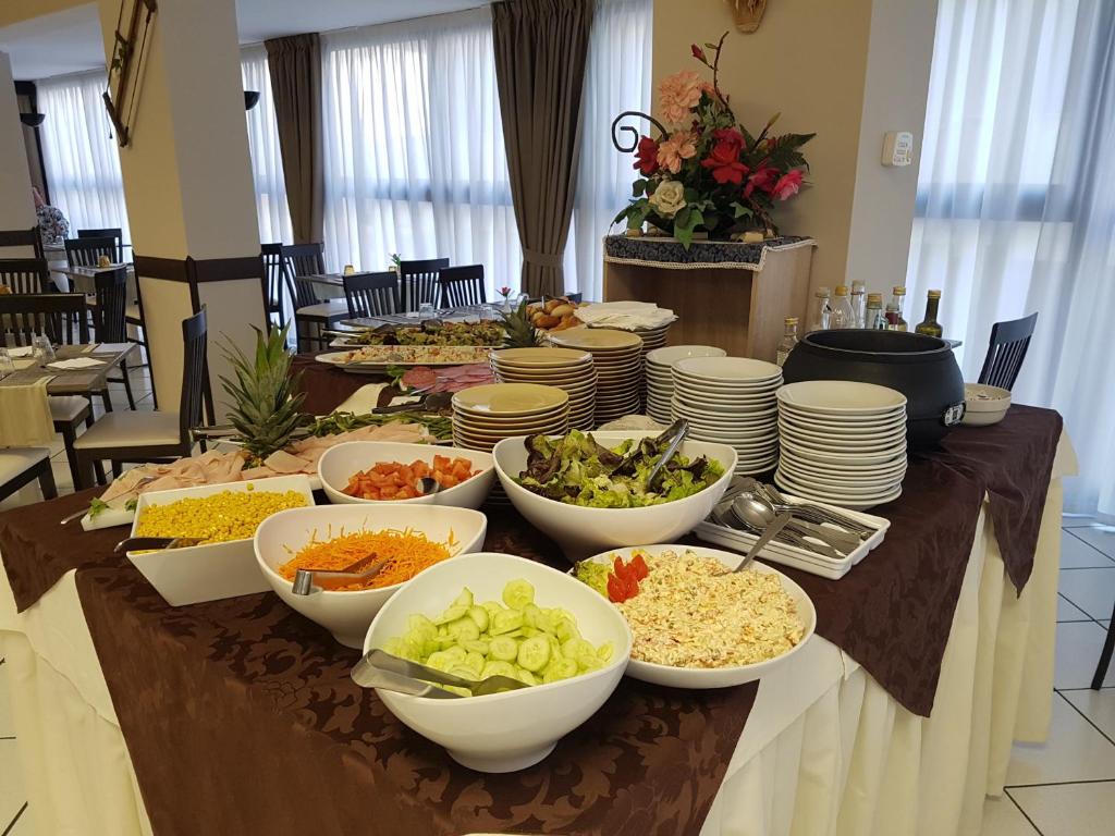 Bufete ar dažādiem salātiem un ēdieniem, tostarp dārzeņiem, augļiem un zupām, izkārtots elegantā restorānā. Kafijas un eļļas pudeles papildina galdu.